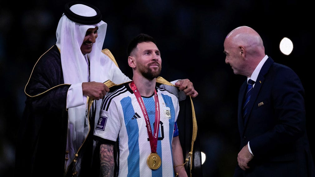 Argentinas lagkapten Lionel Messi får det traditionella klädesplagget bisht av Qatars emir Tamim bin Hamad Al Thani efter VM-finalsegern i söndags. Till höger internationella fotbollsförbundet Fifas president Gianni Infantino.