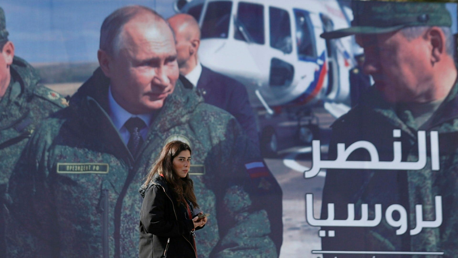 ”Seger åt Ryssland” står det på en affisch med president Putin, som en kvinna går förbi i Damaskus i Syrien.