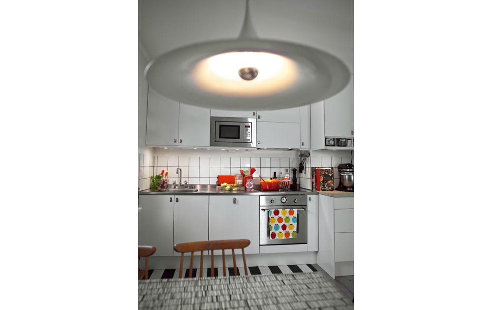 I köket går färgskalan i vitt, orange och svart. Köket är från Ikea. ­Beslagen i gammal stil kommer från Byggfabriken. Lampan ”Semi 60” från Gubi är arv från morfar. Vaxduken ”Zibidie” har Tom Hedquist designat för 10-gruppen.