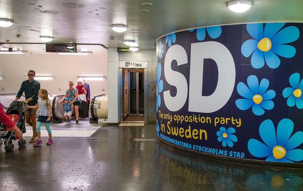 Personer som rör sig på Östermalmstorgs tunnelbanestation möts av bilder på människor som sover på gatan, och i rulltrappan finns budskap som 'Sorry about the mess here in Sweden'.