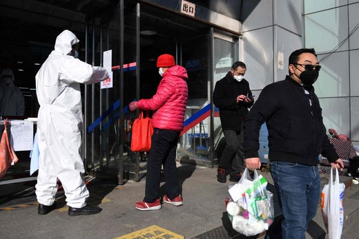 En säkerhetsvakt utanför ett köpcenter i Kina kontrollerar kundernas temperatur, Peking 3 mars.